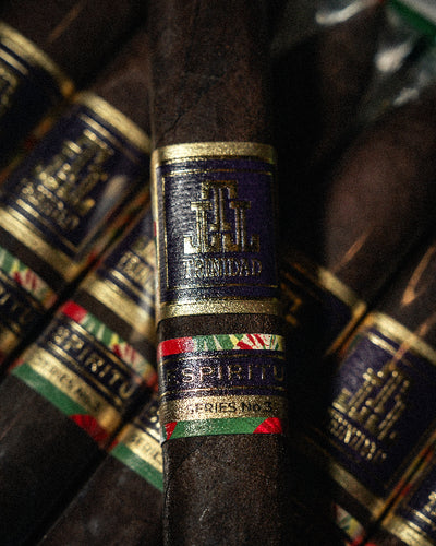 Close-up of a cigar with a brand label against a blurred background of similar cigars.